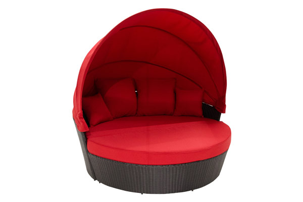 Close-up product view of a Moon Bed from the Moon Bed Collection featuring a deep round wicker base with a dark rattan weave and a retractable canopy. The bed is upholstered in bold red fabric, including a thick circular cushion and four matching square back pillows arranged under the raised canopy. The smooth arching canopy curves over the seating area, creating a shaded, cocoon-like retreat for backyard relaxation.