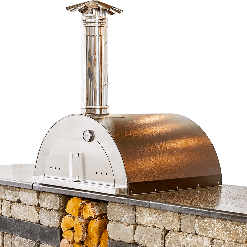Angled view of the Quarry Stone Compact Pizza Oven showcasing the elegant hammered copper finish of the dome-shaped Nonno Peppe oven set atop a textured light beige and charcoal stone base. The oven features a stainless steel front with a polished door, built-in thermometer, and tall chimney capped with a decorative steel vent. Beneath the granite-look countertop, stacked firewood fills the storage cavity, emphasising the oven’s practical and aesthetic balance. The design illustrates compact sophistication ideal for outdoor kitchens, built to blend seamlessly with other modular kits for cohesive backyard living.