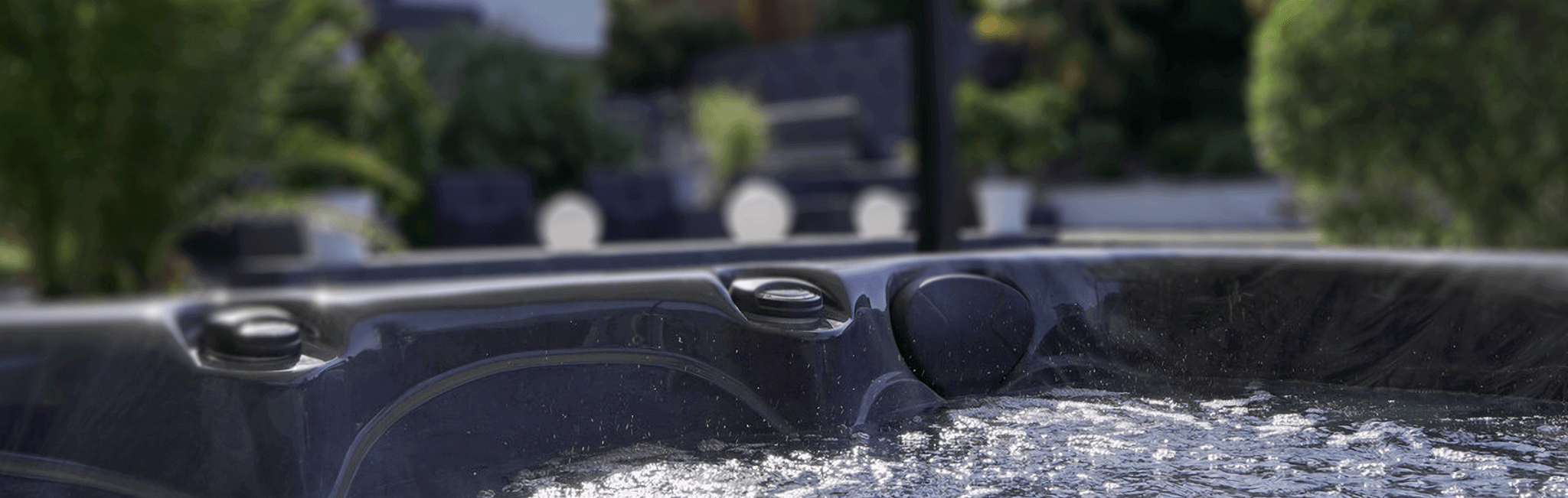 Close-up view of a Maple Spas M420 hot tub filled with bubbling water, showcasing a dark marbled interior finish, cushioned headrest, and contoured seating, with a blurred modern garden patio in the background providing a relaxing outdoor ambiance.