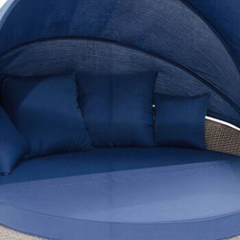 Close-up of the Moon Bed Collection in the blue fabric colour option, showing a large circular cushioned base with matching curved canopy overhead. The cushions and canopy are upholstered in a deep navy blue fabric, creating a cool, modern look. The woven wicker base is slightly visible at the sides, adding texture and contrast to the smooth blue upholstery. The grey border in the image is not part of the product.
