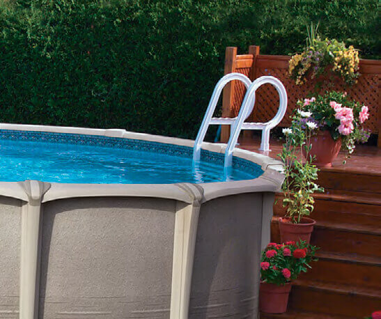 White metal deck ladder with curved handrails descending into a round above ground swimming pool, connected to a wooden deck surrounded by potted flowers and greenery. Designed for secure pool access from a raised deck.