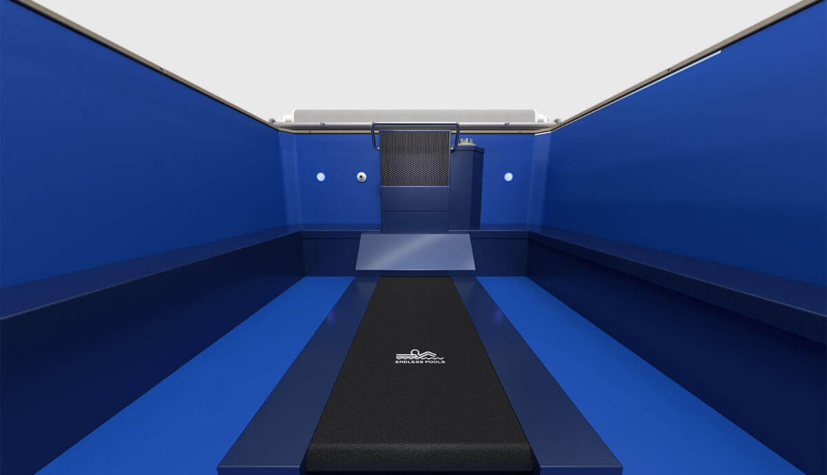 Interior swim-lane view of the Endless Pools EP508 modular pool, featuring the central Hydrodrive™ propulsion system at the far end, flanked by underwater LED lights. The lane includes an integrated black aquatic treadmill mat branded with the Endless Pools logo, extending along the pool floor for low-impact exercise, with wide bench seating running along both side walls.