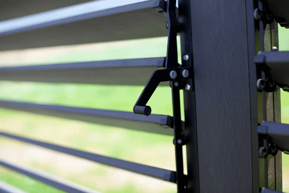 Close-up of the Napa Gazebo’s adjustable louver system, showing the black horizontal slats and their metal handle mechanism for opening and closing. The sturdy vertical support frame is visible on the right, with green blurred lawn in the background.