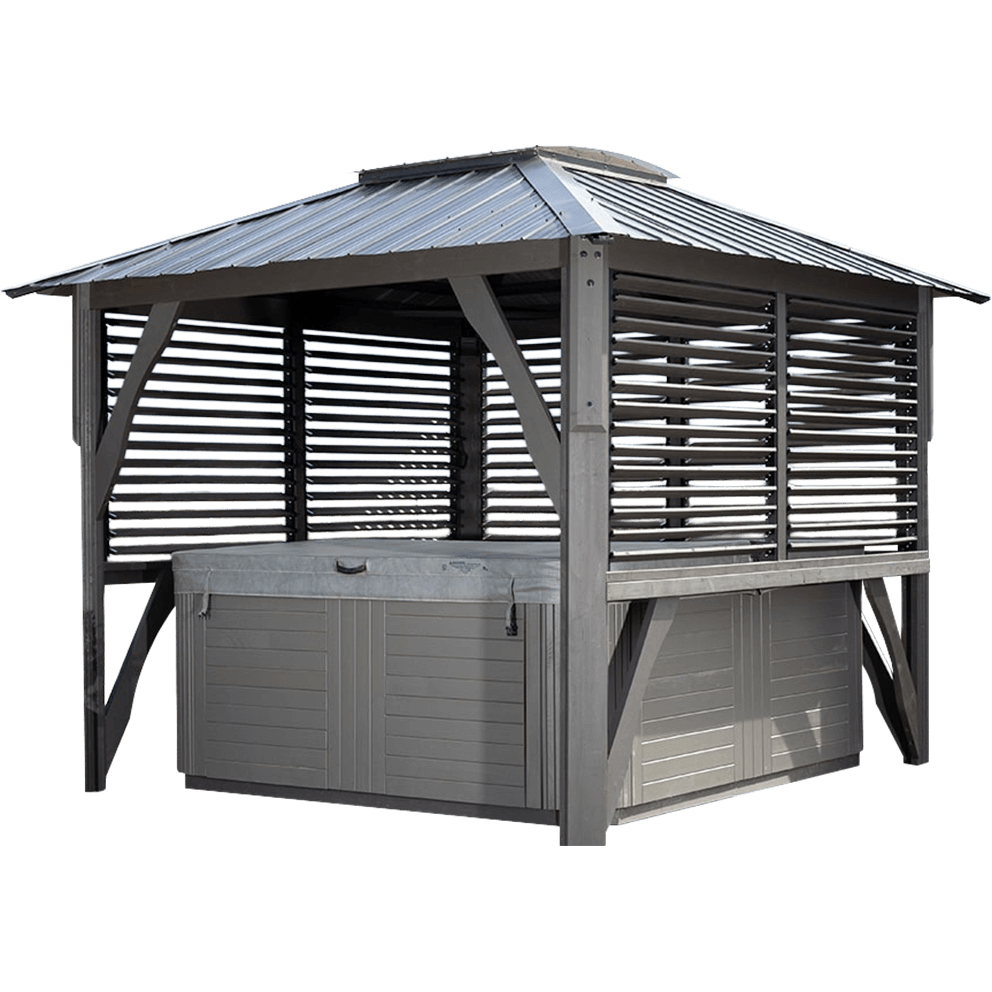 A freestanding Napa Gazebo with a dark gray metal roof featuring a central square skylight dome. The gazebo encloses a rectangular spa with a light gray exterior panel finish. The structure is supported by four sturdy posts with diagonal braces, and the side and rear walls consist of horizontal adjustable metal louvers, partially open to allow light and air through. The foreground shows the raised wooden deck floor, and the background features evergreen trees and mountain scenery.