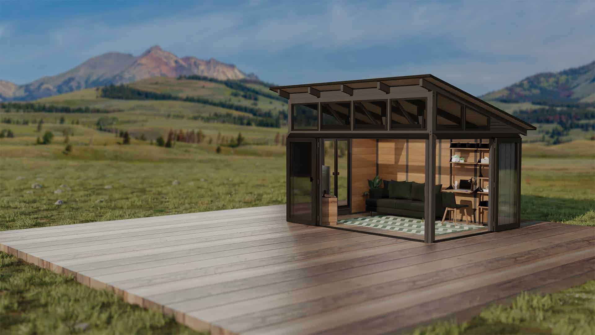 Freestanding Oslo Gazebo placed on a raised wooden platform in a mountain landscape. The structure’s dark framing contrasts with its warm wooden siding and large glass panels, while the interior features a modern sofa and open shelving, styled like a home office or lounge space.