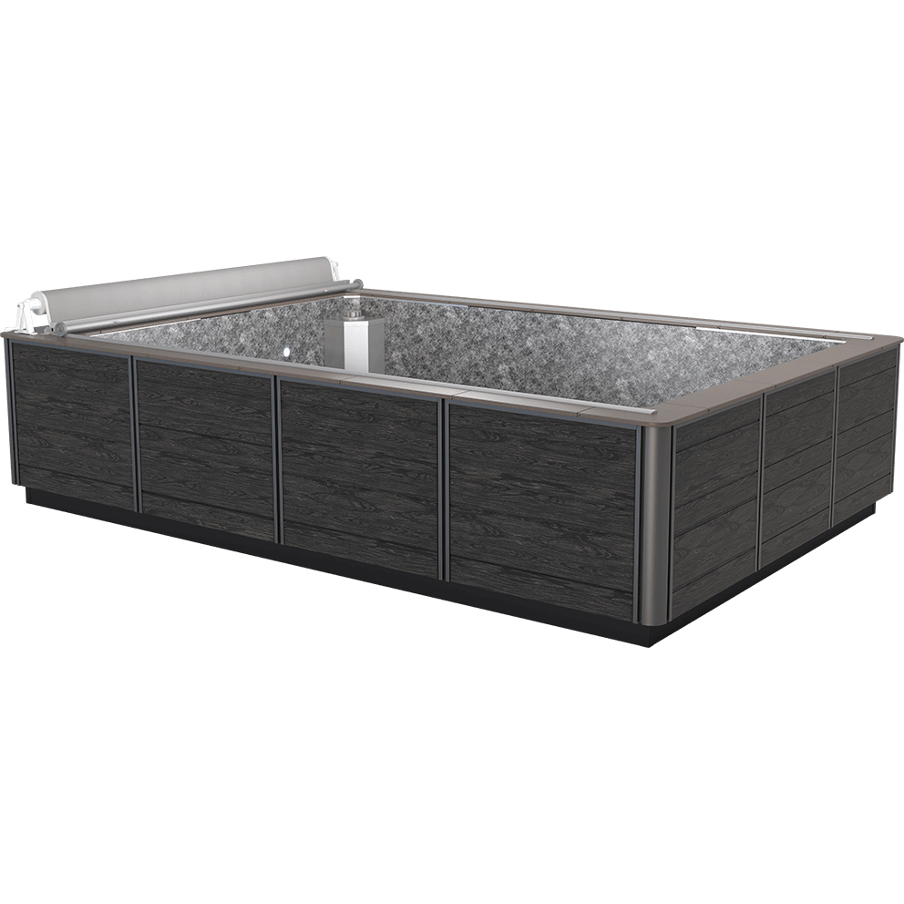 Front corner view of the Endless Pools Plunge Max Therapy Pool, showing a large, rectangular, modular above-ground pool with dark grey wood-effect exterior panels framed by vertical silver-metal trim. The wide coping around the rim is a light taupe colour, creating a smooth contrast with the dark side panels. Inside, the pool shell has a speckled grey finish. At the far end, built into the wall, is a large silver-metal propulsion housing flush with the interior, positioned centrally, with an integrated rectangular water return area. The pool has a fully rolled-up retractable grey safety cover mounted along the near-side coping, extending the full width.