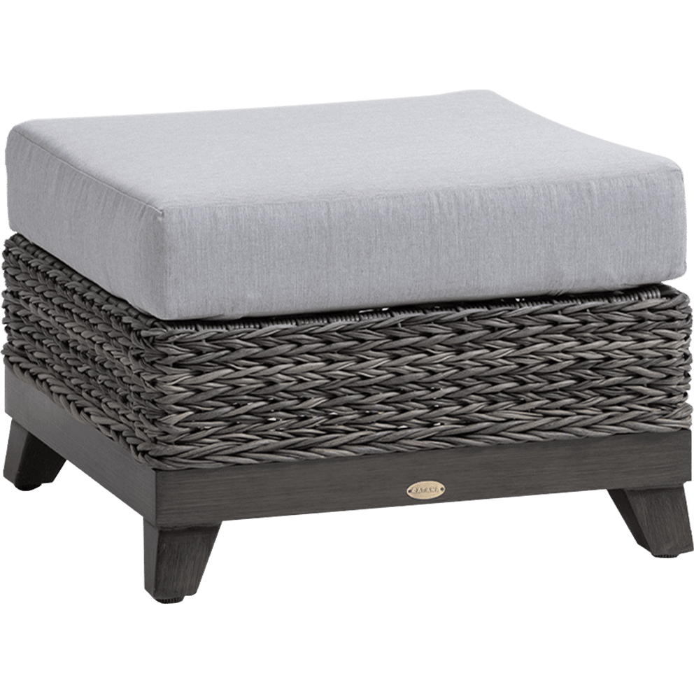 Outdoor Asheville Collection ottoman shown in an angled view, featuring a thick, rectangular, light grey Sunbrella cushion on top of a woven resin wicker base in a weathered slate grey finish. The wicker has a hand-braided texture with subtle depth and shading, resting on short tapered legs made of durable cast aluminium with a dark wood-like finish. A small oval brand medallion is visible on the front frame.