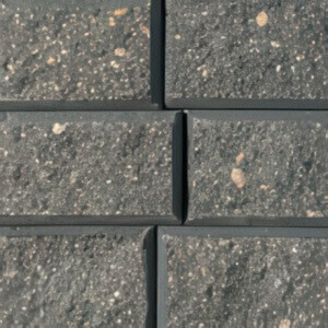Close-up of the StackStone® Fire Pit concrete blocks in the Charcoal colour option. The image shows tightly stacked rectangular stones with a deep charcoal-grey tone, featuring subtle speckles of lighter grey and tiny mineral inclusions that add a natural, textured appearance. Each block has slightly bevelled edges, creating defined joints that enhance the depth and dimensionality of the masonry surface.