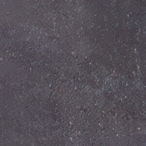 Close-up of the Ebony colour option for the Caliber Stone Fire Pit, showing a dark blackened concrete surface with subtle blue-grey undertones and fine speckling throughout. The texture is smooth yet slightly granular, giving the stone a refined yet natural appearance reminiscent of cooled volcanic rock.