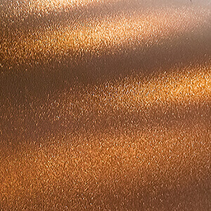Close-up of the Hammered Copper colour option for the oven unit of the Quarry Stone Compact Pizza Oven, showing a textured metallic surface with a shimmering copper finish. The surface reflects light in subtle gradients of bronze and gold tones, giving it a handcrafted, artisanal appearance reminiscent of forged metalwork with fine hammer marks that add depth and warmth.