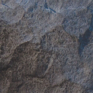 Close-up of the Ebony Accent colour option for the Quarry Stone Fireplace and Quarry Stone Compact Pizza Oven, showing a deep charcoal-black textured surface with blue-grey highlights and rugged natural stone detail. The uneven, cratered texture and tonal variations capture the essence of hand-hewn rock, lending a striking contrast and sophisticated depth to fireplace designs.