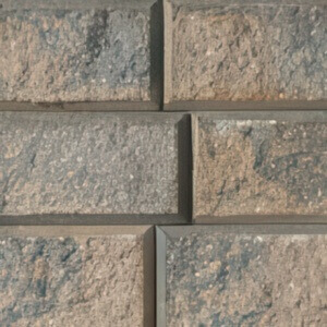 Close-up of the StackStone® Fire Pit concrete blocks in the Sierra Grey colour option. The image reveals a warm blend of grey and earthy brown hues across rectangular, rough-textured blocks with visible aggregates and natural tonal variations. The slight bevel along the edges adds visual structure, highlighting the handcrafted, weathered aesthetic typical of Barkman’s Sierra Grey finish.