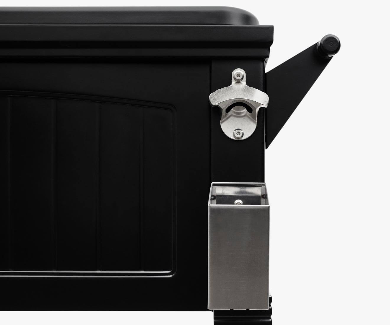 Detailed close-up of the Permasteel 80qt Furniture Style Cooler in black, focusing on the stainless steel bottle opener and rectangular cap catcher mounted near the upper right edge. The cooler’s vertical panel embossing and powder-coated matte finish are clearly visible, conveying durability and refined craftsmanship ideal for outdoor gatherings.