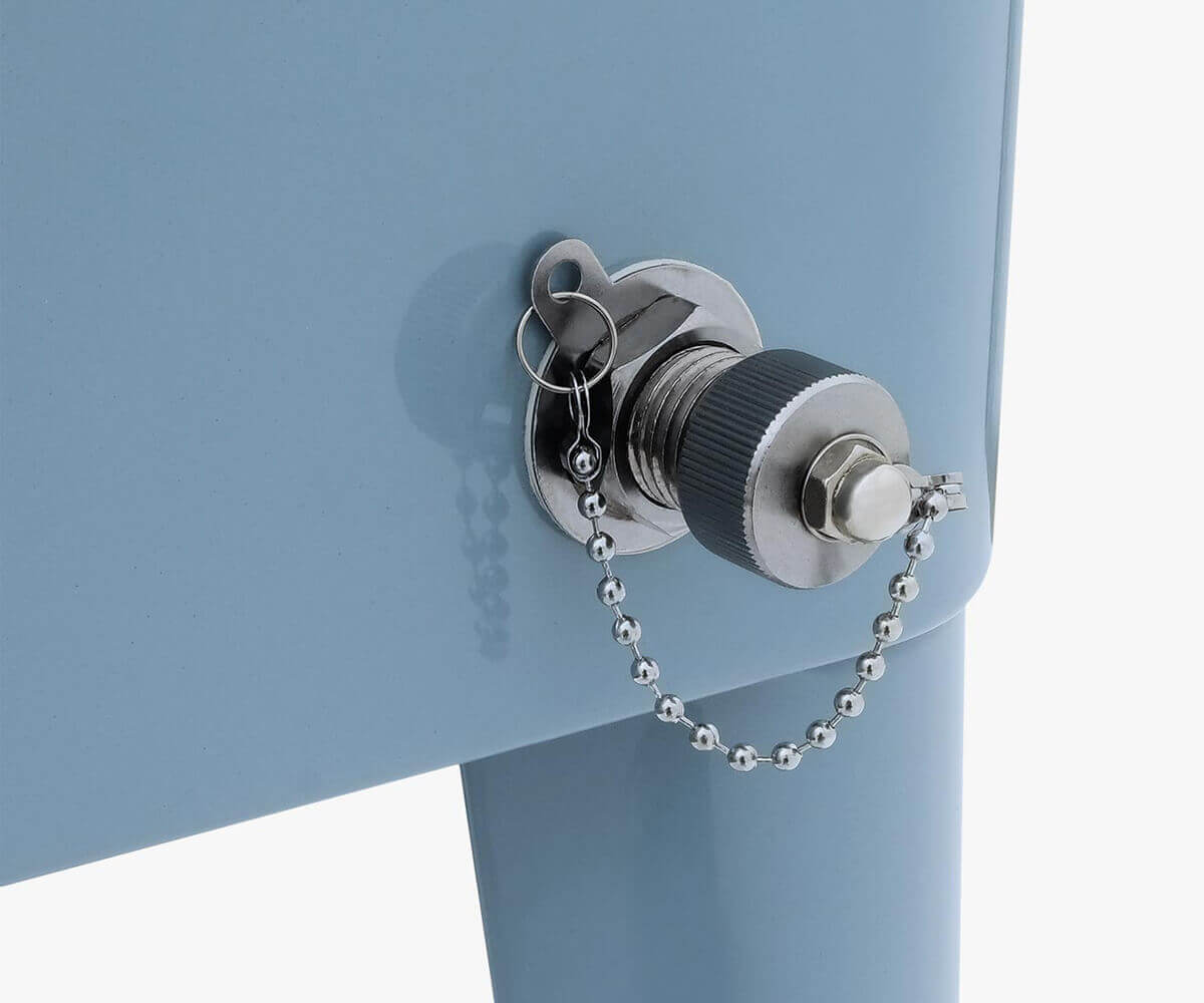 Extreme close-up of the Permasteel 80qt cooler’s drain plug and chain assembly, located near the lower right corner of the cooler’s body. The chrome drain plug features a textured grip cap attached by a short metal bead chain, ensuring easy removal and secure closure. The surface of the cooler has a smooth light-blue finish, demonstrating the attention to detail in both design and functionality.