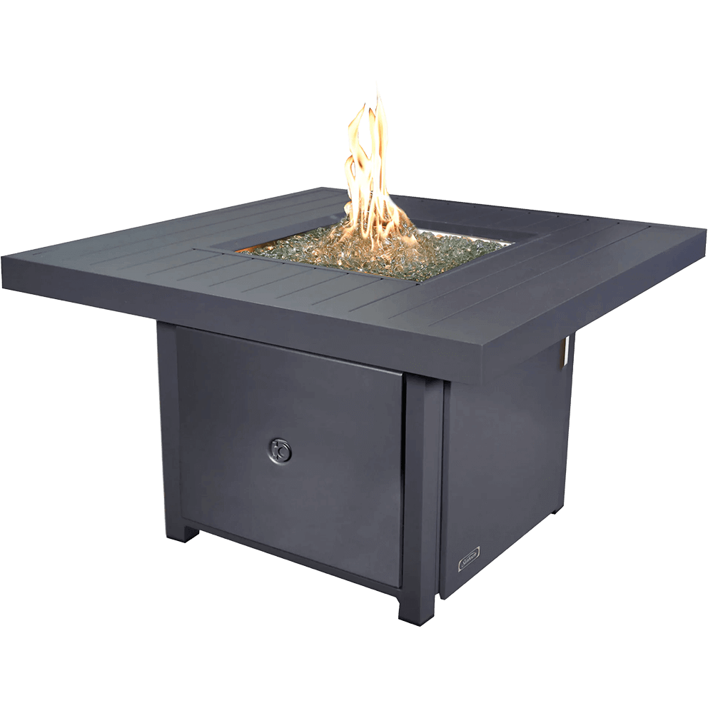 An angled product view of the Sunbeam Fabia Fire Table showcasing its warm grey slatted aluminum tabletop and central recessed burner filled with sparkling kidney shaped glass beads. Tall amber flames rise evenly from the stainless steel burner, highlighting its 50,000 BTU output. The square table base features a flush front access panel for the propane tank, and the overall structure presents a clean, modern silhouette with precise edges and subtle metallic texture.