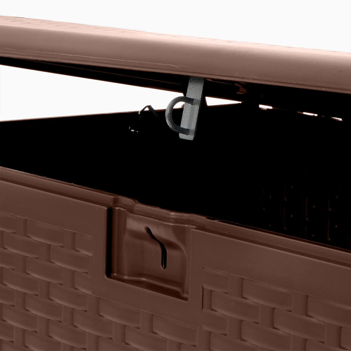 Close-up of the PDG 73 Gallon Resin Outdoor Storage Deck Box lid latch mechanism. The image focuses on the metal loop attached beneath the lid, aligned directly above the resin latch opening on the front panel. The wicker-patterned exterior surrounds the latch cut-out, showing the locking slot’s textured perimeter and the moulded frame supporting the latch area.