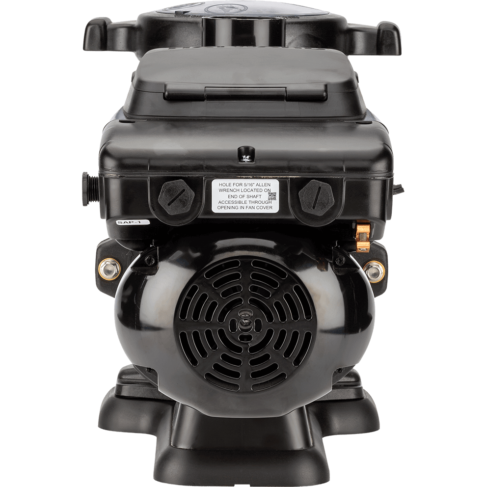 Rear facing view of the Hayward TriStar VS Variable-Speed Pool Pump, isolated on a transparent background, centred on the motor end bell and fan cover. The circular black fan grille fills the lower middle with concentric vent openings, while above it a wide rectangular control enclosure sits like a cap, its lid closed and a white caution label centred on the front face. Two large round screw cap fittings protrude horizontally from the left side of the control box face, and a copper coloured bonding lug and small hardware sit on the right front corner. The wet end is mostly hidden behind, but the top of the strainer lid and the vertical discharge outlet are faintly visible above the control housing. The base feet are visible at the bottom left and right, creating a stable stance.