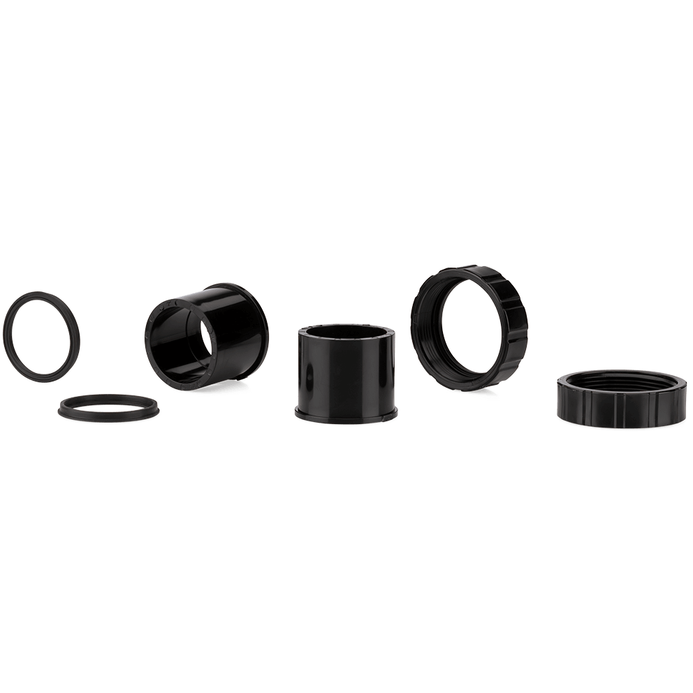 Wide layout view of Hayward TriStar VS Variable-Speed Pool Pump union and seal components, isolated on a transparent background, arranged in a straight line from left to right. Two thin black O rings sit at the far left, followed by a black flat gasket ring and a short black tailpiece. At centre, a taller black coupling piece stands upright. To the right, two larger threaded union nuts face inward with their internal threads visible, and a final wide ring sits at the far right, showing the full connection kit separated into individual parts for assembly.