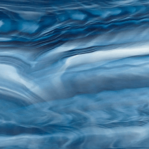Close-up view of the Ocean Wave Opal acrylic colour option for Cal Spas hot tubs, swim spas, and cold plunges, featuring a fluid blend of ocean-inspired blues ranging from deep navy to soft sky blue. The surface displays sweeping, wave-like marbling with layered, translucent patterns and soft white opalescent highlights that resemble moving water. Gentle gradients and flowing lines create depth and motion across the acrylic, while the glossy finish enhances the luminous, glass-like quality, delivering a serene and immersive aquatic aesthetic.