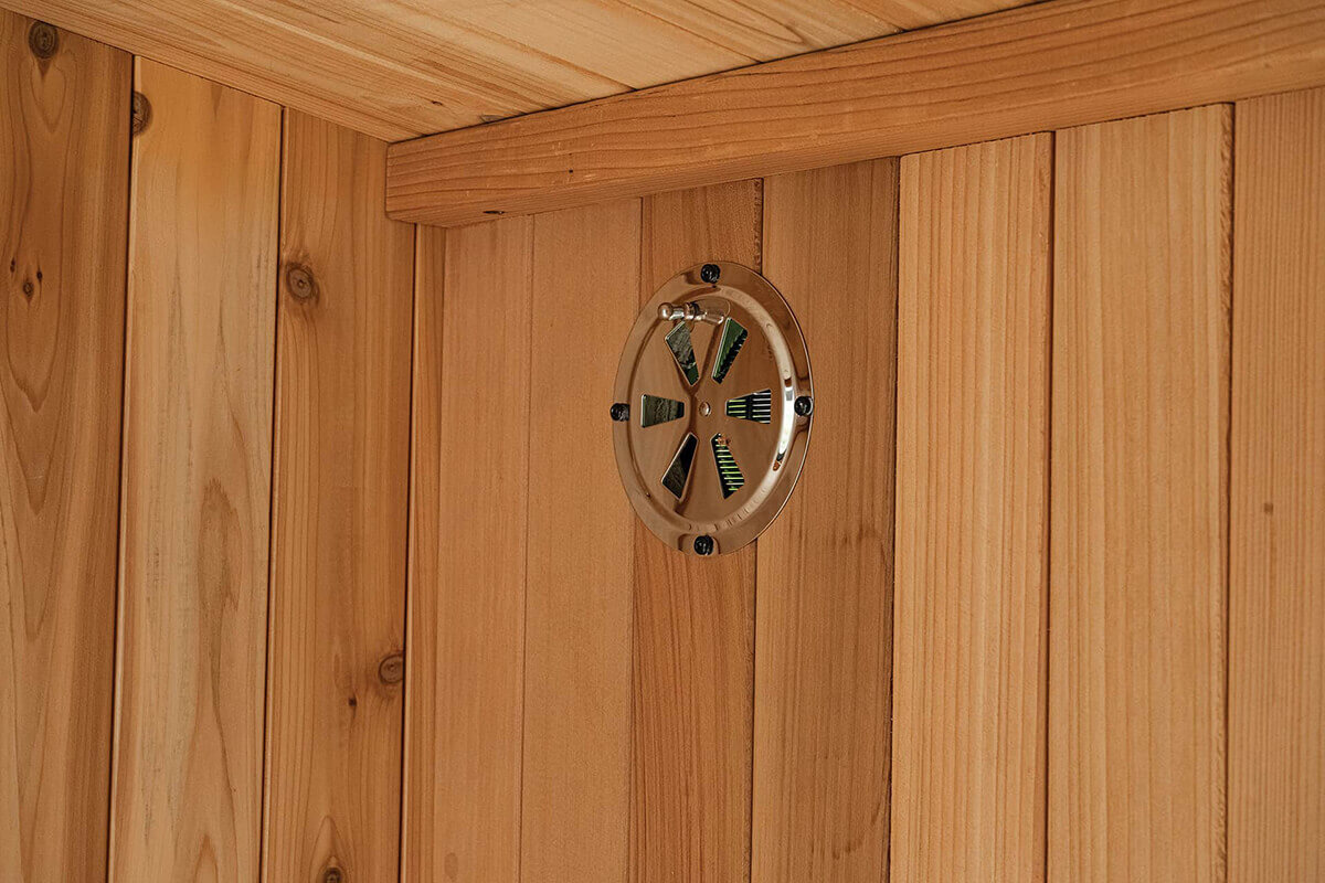 Visscher Luxe Sauna ventilation: Interior close-up of the metallic circular wall vent mounted on natural Western Red Cedar planks for air exchange.
