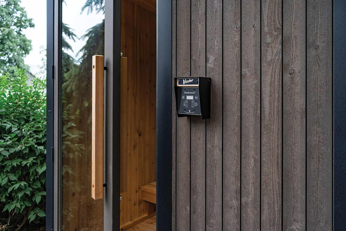Visscher Luxe Sauna exterior: Close-up of grey-brown cladding, branded nameplate, and glass door revealing the warm-toned Western Red Cedar interior.