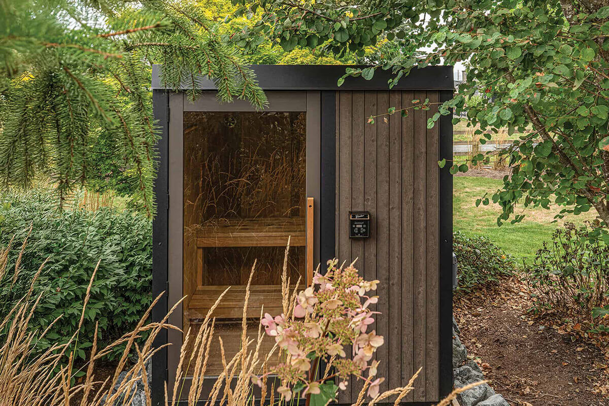 Visscher Luxe Sauna in Winnipeg: Straight-on garden view featuring the large glass door, cedar benches, and Homecraft controls in a lush setting.
