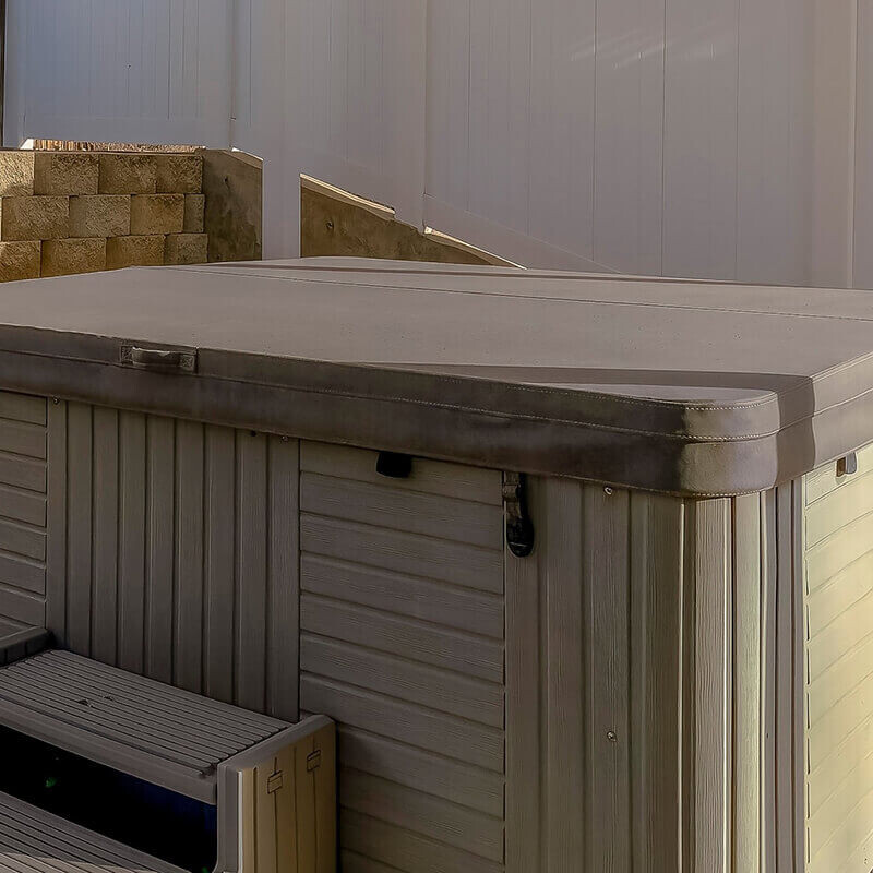 Light grey marine grade vinyl hot tub cover fitted on an outdoor spa with steps and side lifter hardware.