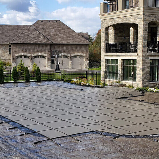 Installed grey PSP Pool Safety Cover fitted over a custom in-ground pool on a stone patio with deck tension straps.