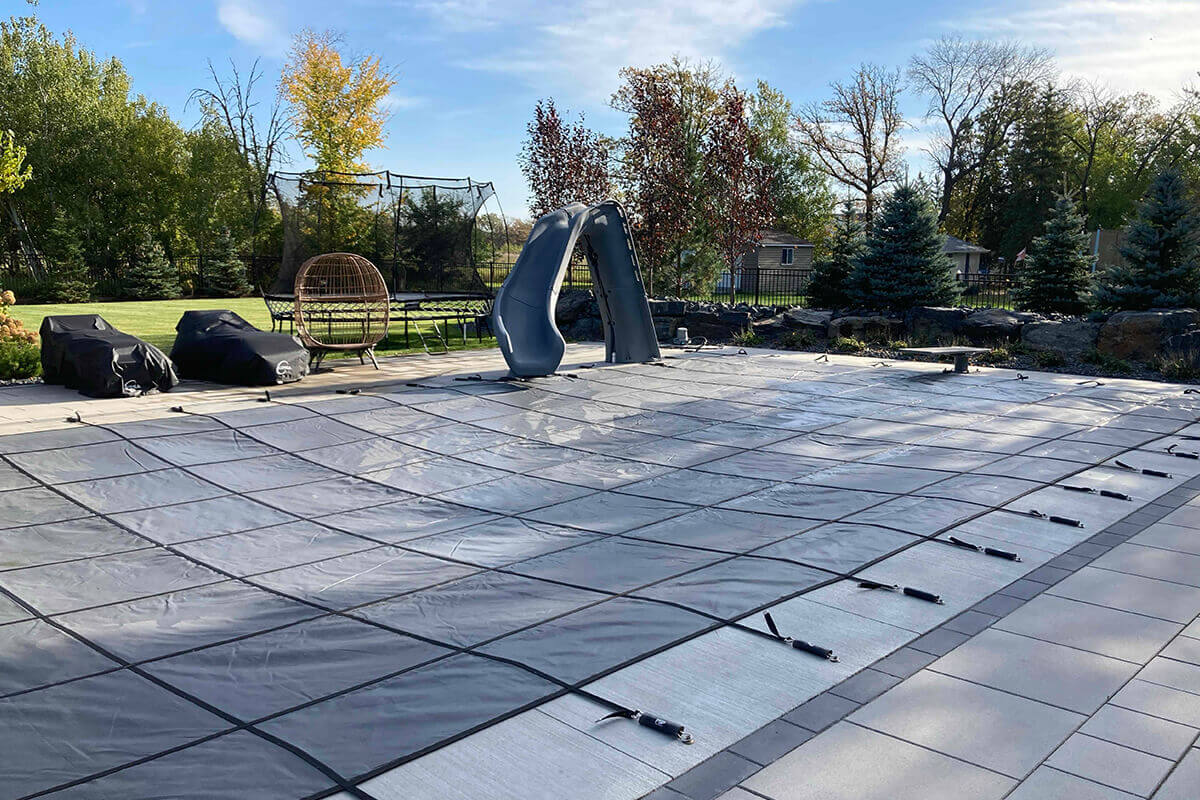 Installed grey mesh PSP Pool Safety Cover with black grid webbing over an in-ground pool on a stone patio.